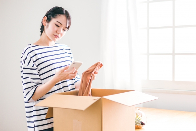 段ボールの荷物をスマホで確認する女性